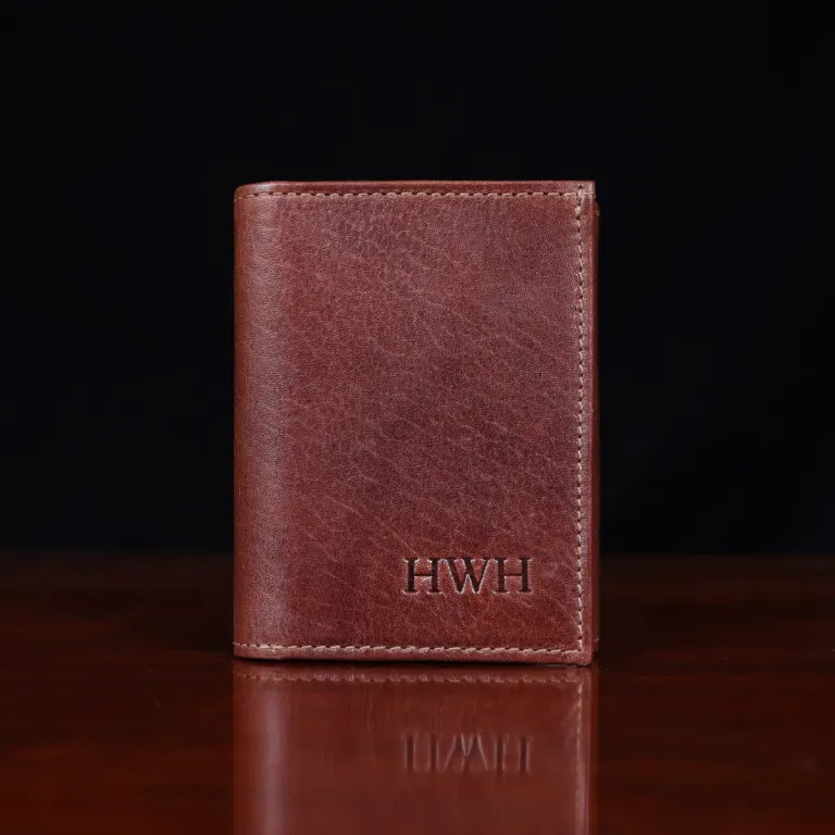no 1 trifold wallet in brown steerhide on a wooden table with a dark background - front view