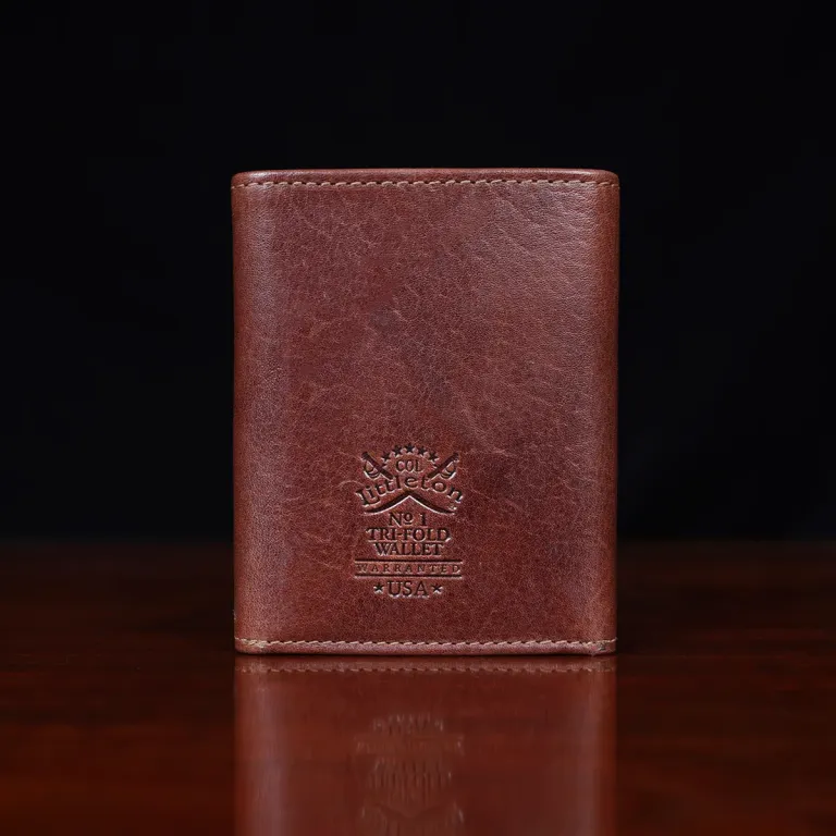 no 1 trifold wallet in brown steerhide on a wooden table with a dark background - back view